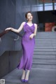 A woman in a purple dress leaning against a wall.