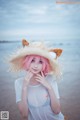 A woman with pink hair wearing a straw hat on the beach.