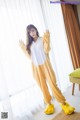 A woman in a yellow and white pajamas standing in front of a window.