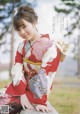 A woman in a red and white kimono sitting on a rock.