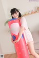 A woman in a pink dress holding a giant inflatable pillow.