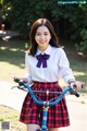 A woman in a school uniform holding a blue bike.