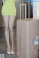 A woman in a yellow dress standing next to a pink suitcase.